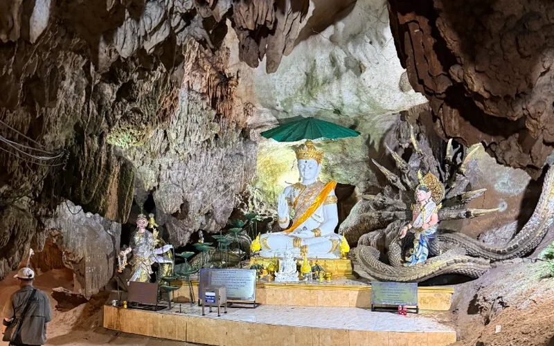 White seated Buddha shrine with a green ceremonial umbrella inside Chiang Dao Cave.