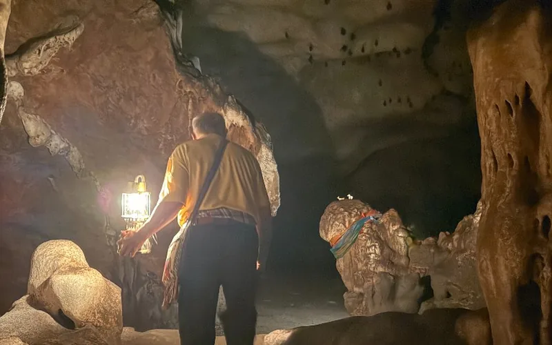 Guide carrying a bright gas lantern through a dark chamber of Chiang Dao Cave, with bats on the ceiling above.