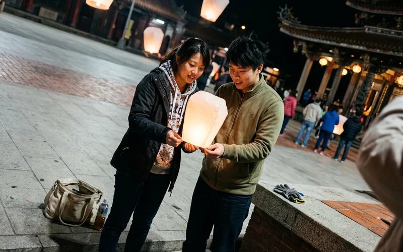 People releasing a lantern beside a temple at night