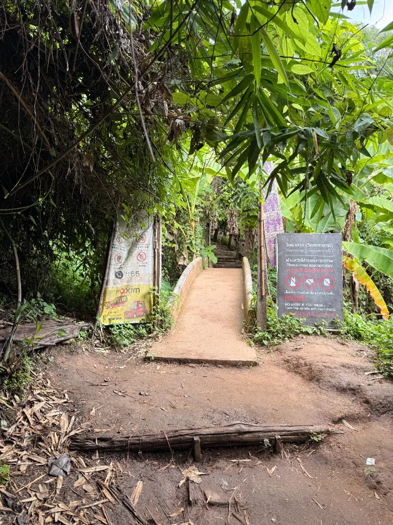 Concrete bridge approach to Wat Pha Lat with a dress-code sign beside the path.