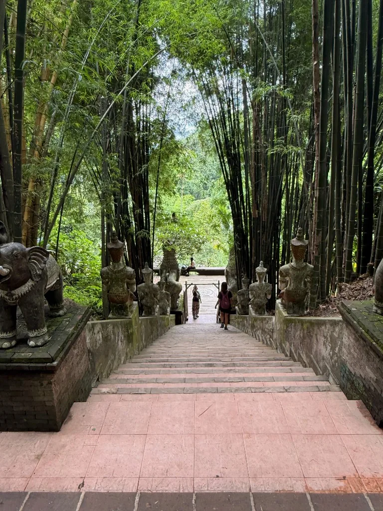 Stone staircase flanked by guardian statues and bamboo leading into Wat Pha Lat.