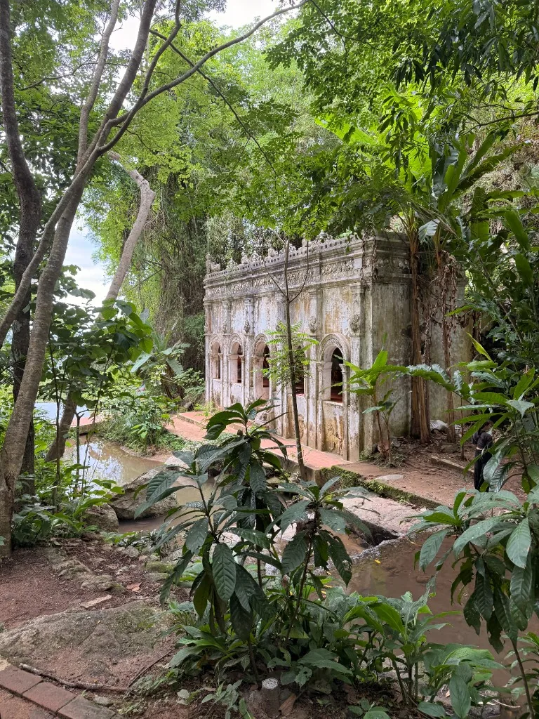 Weathered stone temple building beside a stream in forest at Wat Pha Lat.