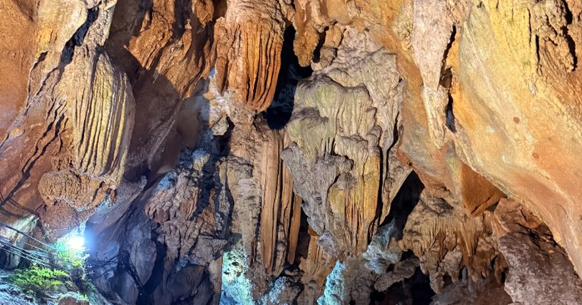 Visitors on a lit concrete walkway inside Chiang Dao Cave beneath large stalactites and rock formations.